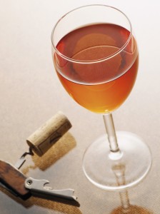 Glass of rose wine beside a corkscrew with a cork