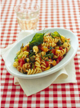Piatto di fusilli alla campana con verdure, appoggiato su un tavolo con tovaglia a quadretti bianchi e rossi