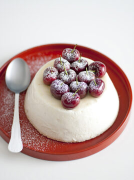 Dessert al cucchiaio tipo spumone o bavarese bianca a forma di cupola rovesciata, decorata in superficie con ciliegie intere spolverate di zucchero a velo. 