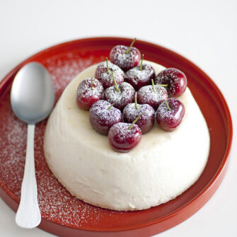 Dessert al cucchiaio tipo spumone o bavarese bianca a forma di cupola rovesciata, decorata in superficie con ciliegie intere spolverate di zucchero a velo. 