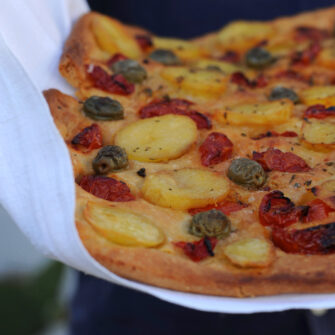 Focaccia barese con mezzi pomodorini, patate, olive verdi e origano