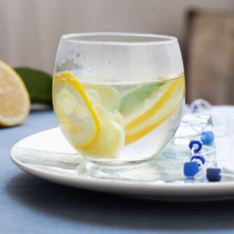 Bicchiere di tisana calda con fette di limone fresco e zenzero, bevanda naturale per la digestione e le difese immunitarie.