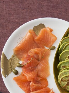 Mini pancake verdi ai piselli su carta accompagnati da salmone affumicato su piatto bianco