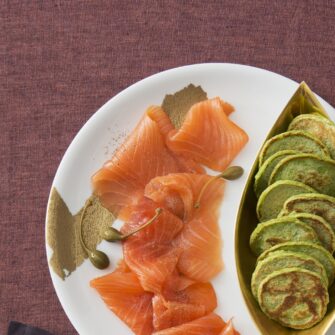 Mini pancake verdi ai piselli su carta accompagnati da salmone affumicato su piatto bianco