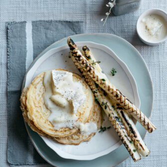 Pancake di avena con sopra camembert fuso, accompagnati da asparagi bianchi grigliati su piatto bianco