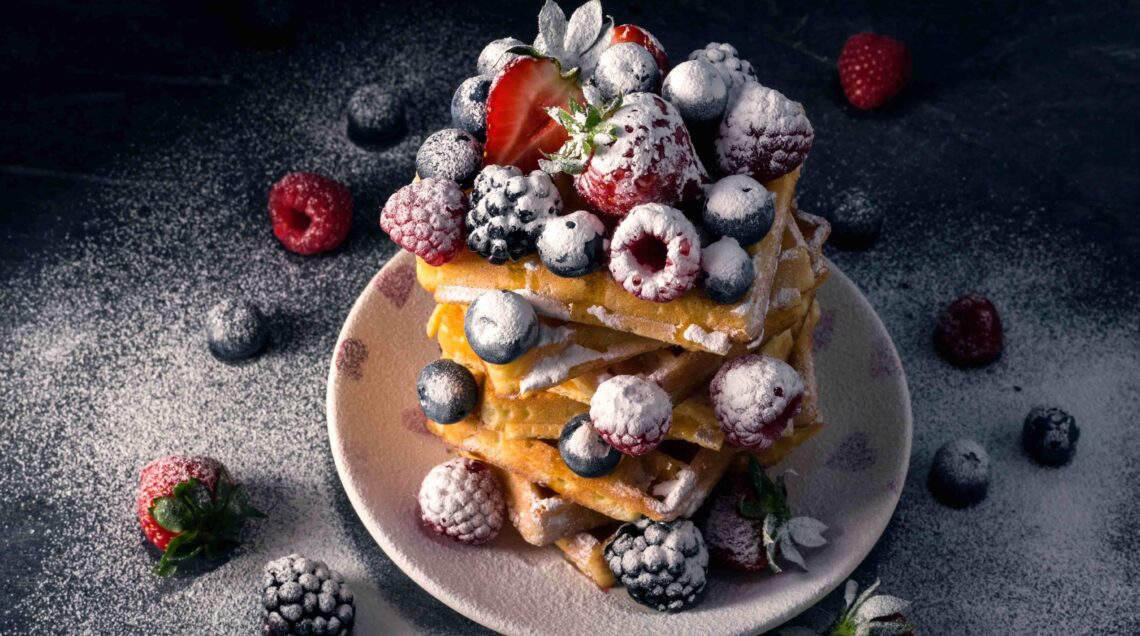 Traditional Belgian waffles with fresh summer berries, blueberry raspberry, strawberry and blackberry with icing sugar.