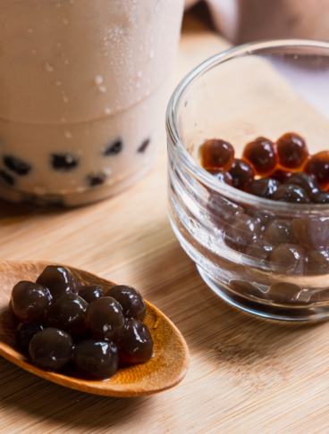 Perle di tapioca scure e gommose cotte con zucchero di canna su un cucchiaio di legno, accanto a un bicchiere di bubble tea.