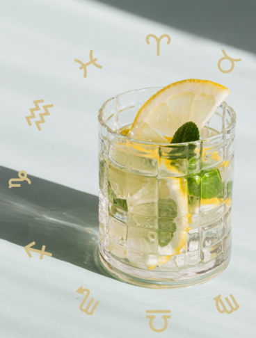 Un bicchiere di cocktail rinfrescante con limone e menta circondato dai simboli dorati dei dodici segni zodiacali.