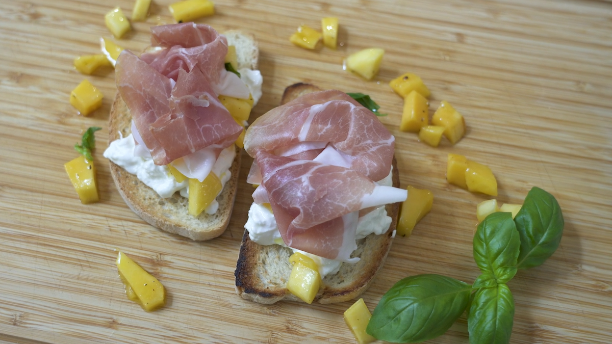 Bruschetta con stracciatella, mango marinato al basilico e prosciutto crudo