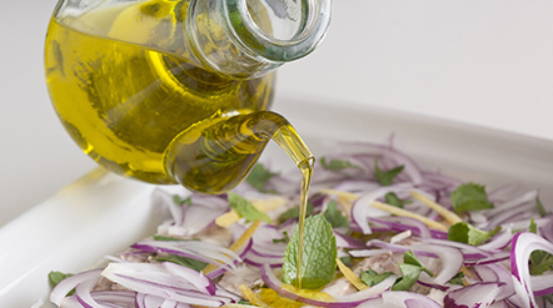 Mano con boccetta d'olio che condisce dei filetti di pesce