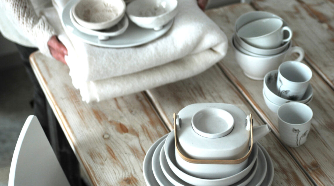 Persona che apparecchia la tavola con tovaglia e stoviglie bianche