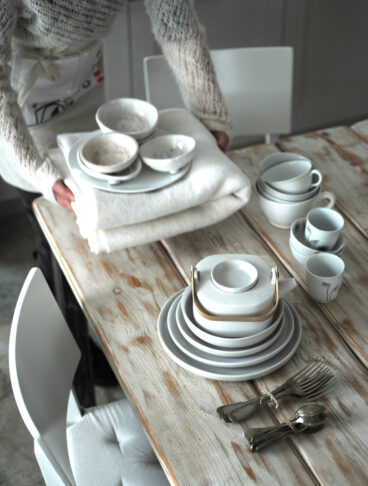 Persona che apparecchia la tavola con tovaglia e stoviglie bianche