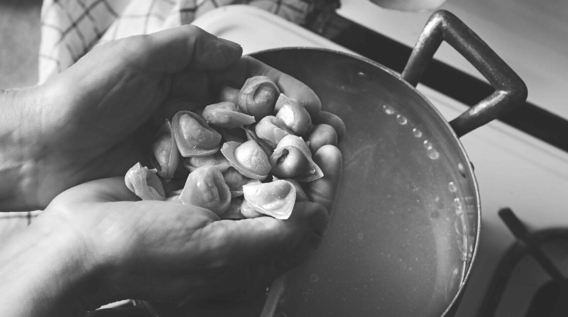 mani che versano tortellini in brodo