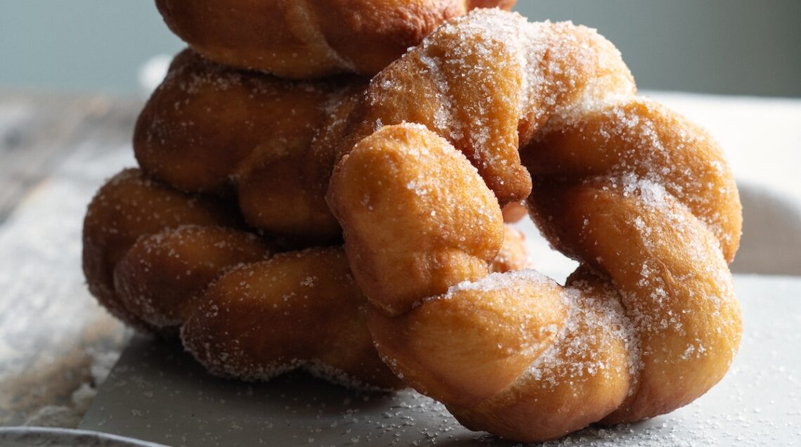 ciambelle intrecciate cosparse di zucchero semolato su piatto bianco