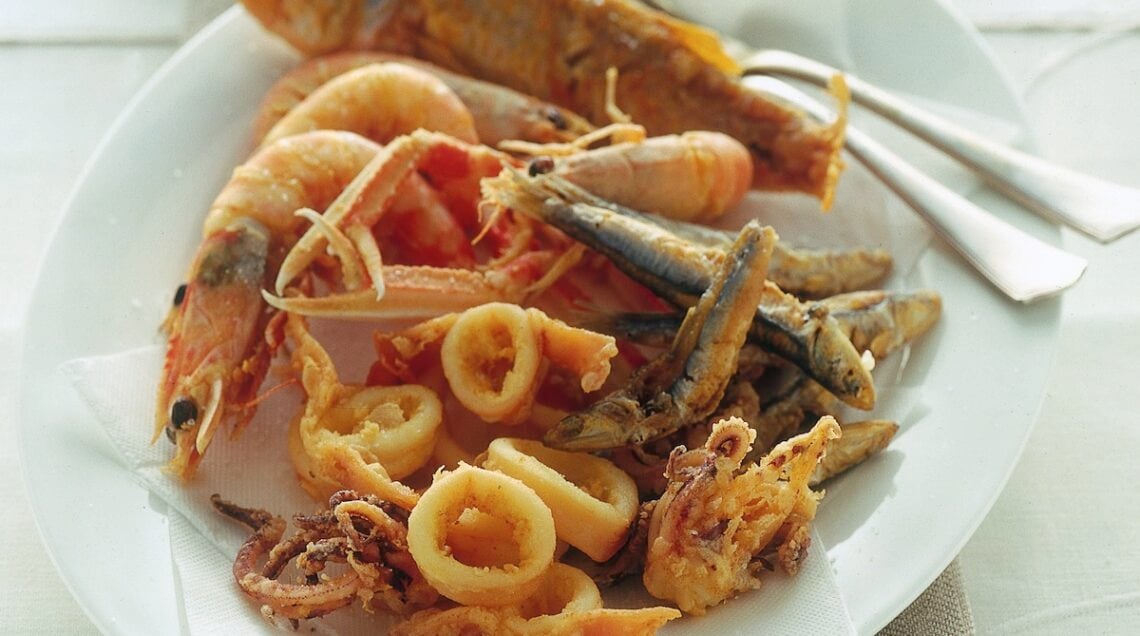 fritto misto di pesce con calamari e gamberi su piatto bianco con posate