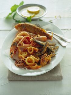 fritto misto di pesce con calamari e gamberi su piatto bianco con posate