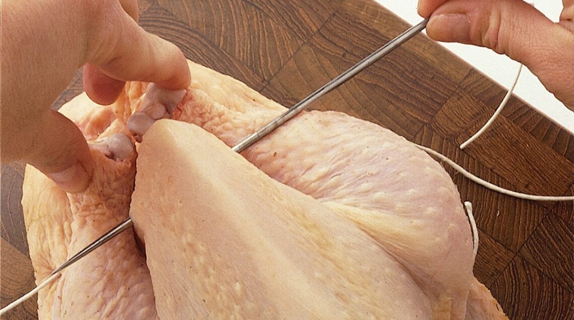 ago che trapassa il pollo crudo in prossimità delle cosce