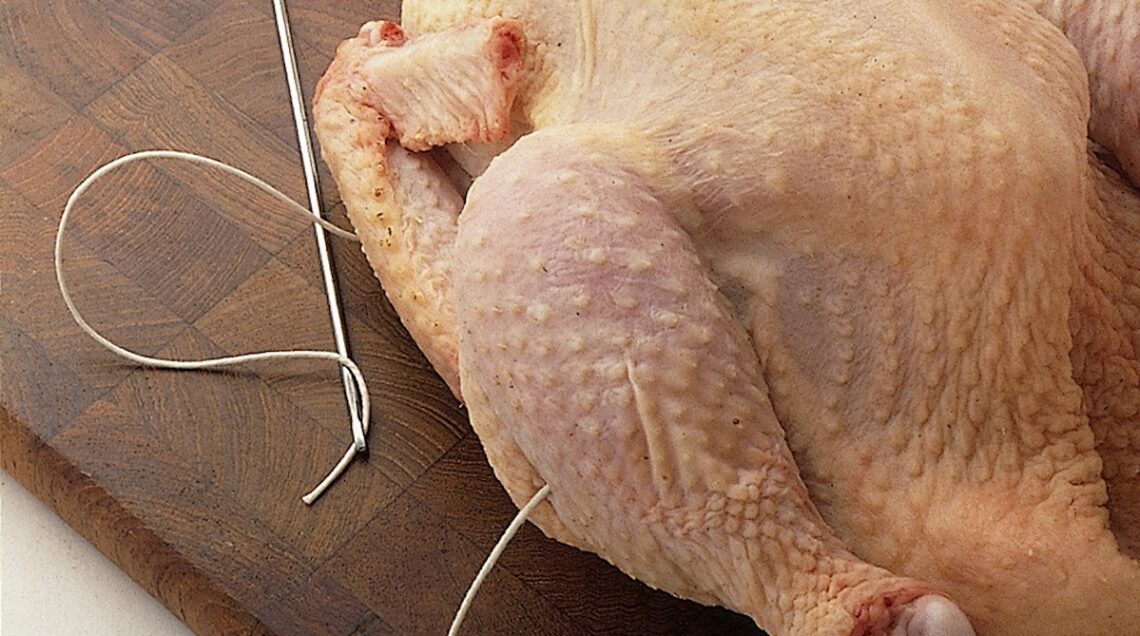 pollo crudo con due lembi di spago che escono dalla coscia e dall'ala