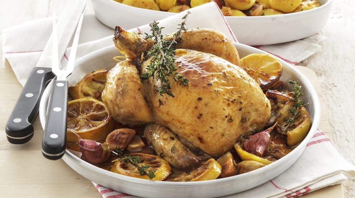 pollo arrosto circondato da fette di limone, spicchi d'aglio e rametti aromatici