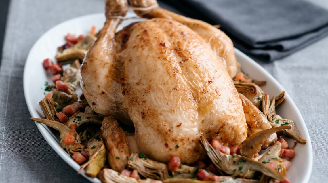 pollo arrosto su un piatto con carciofi e pancetta