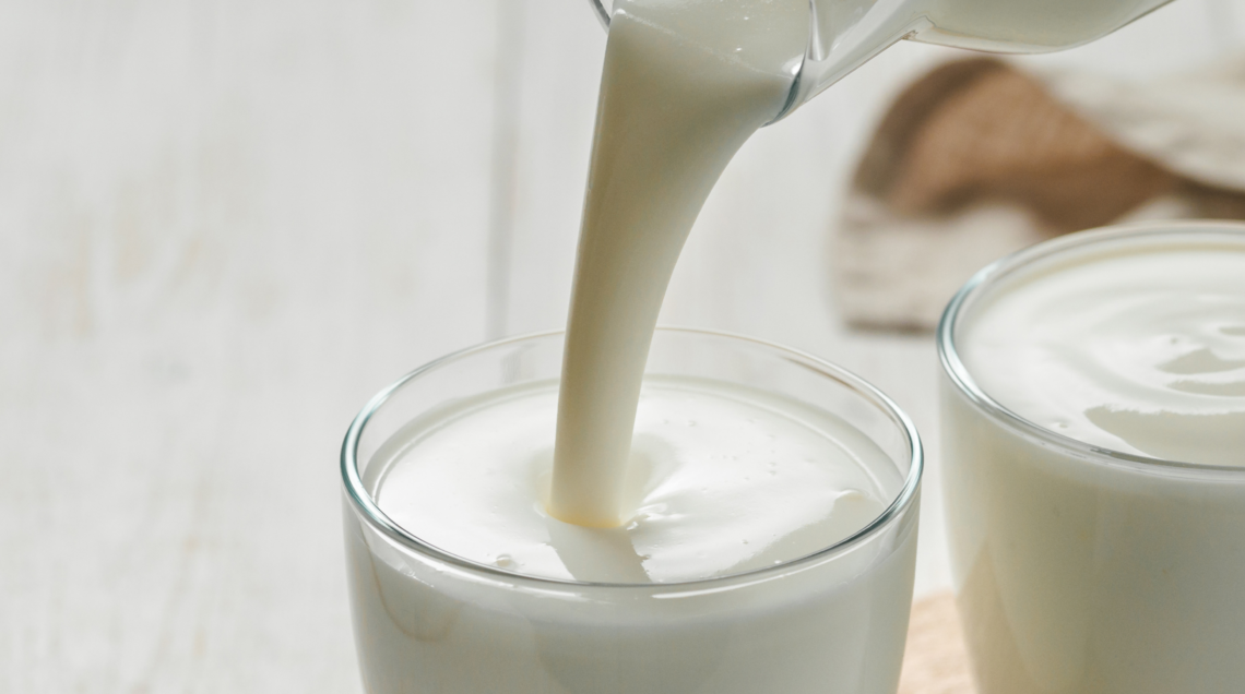 Latte bianco versato in un bicchiere di vetro accanto a una ciotola di yogurt cremoso.