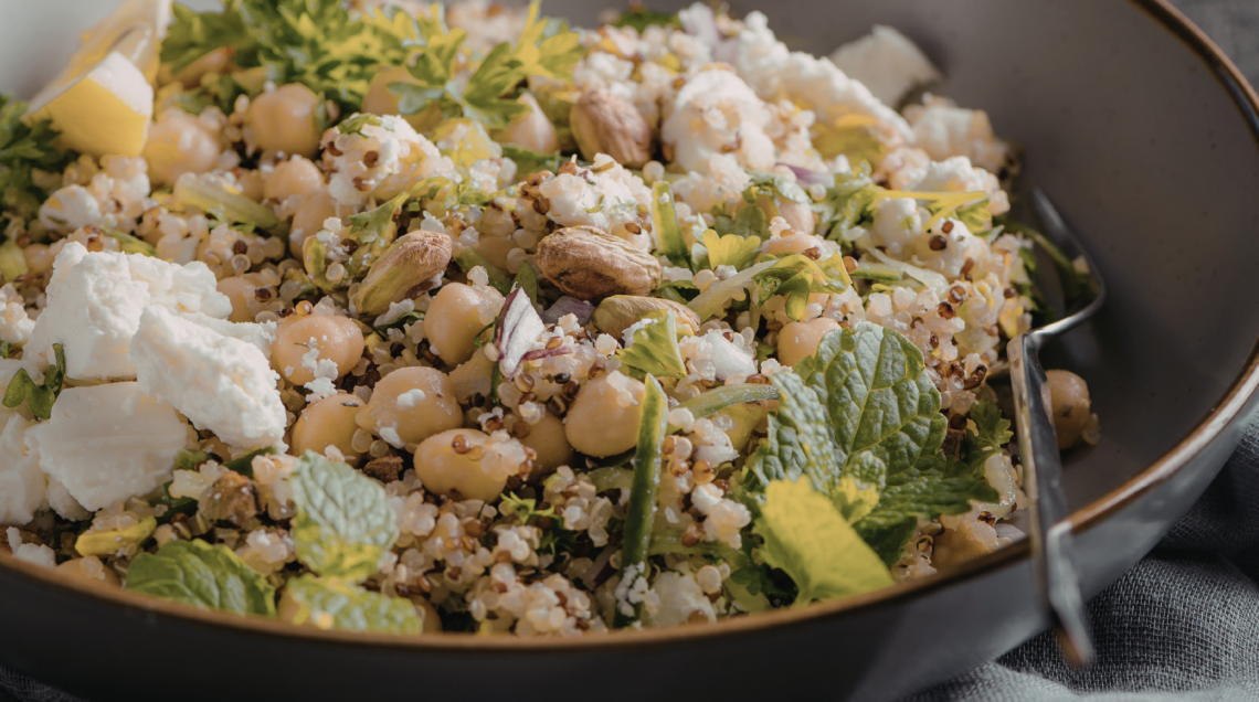 Una ciotola di insalata con quinoa, ceci, cubetti di formaggio feta, pistacchi e foglie di menta fresca.