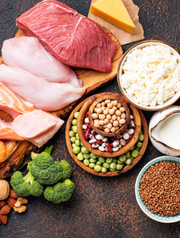 Composizione di carne, pesce, uova, legumi, cereali, latte e frutta secca su sfondo scuro