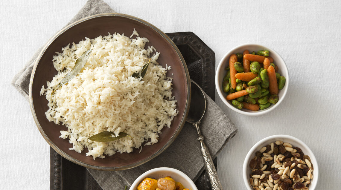 Piatto di riso e ciotole con condimenti di patate, carote e fave, frutta secca