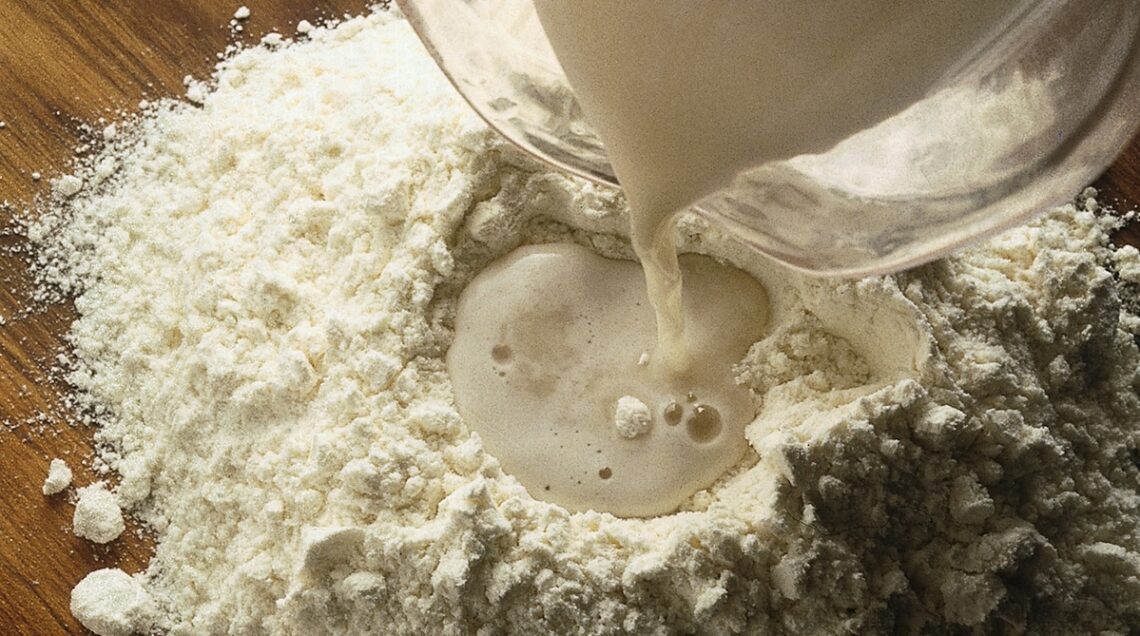 liquido aggiunto alla farina sul piano di lavoro
