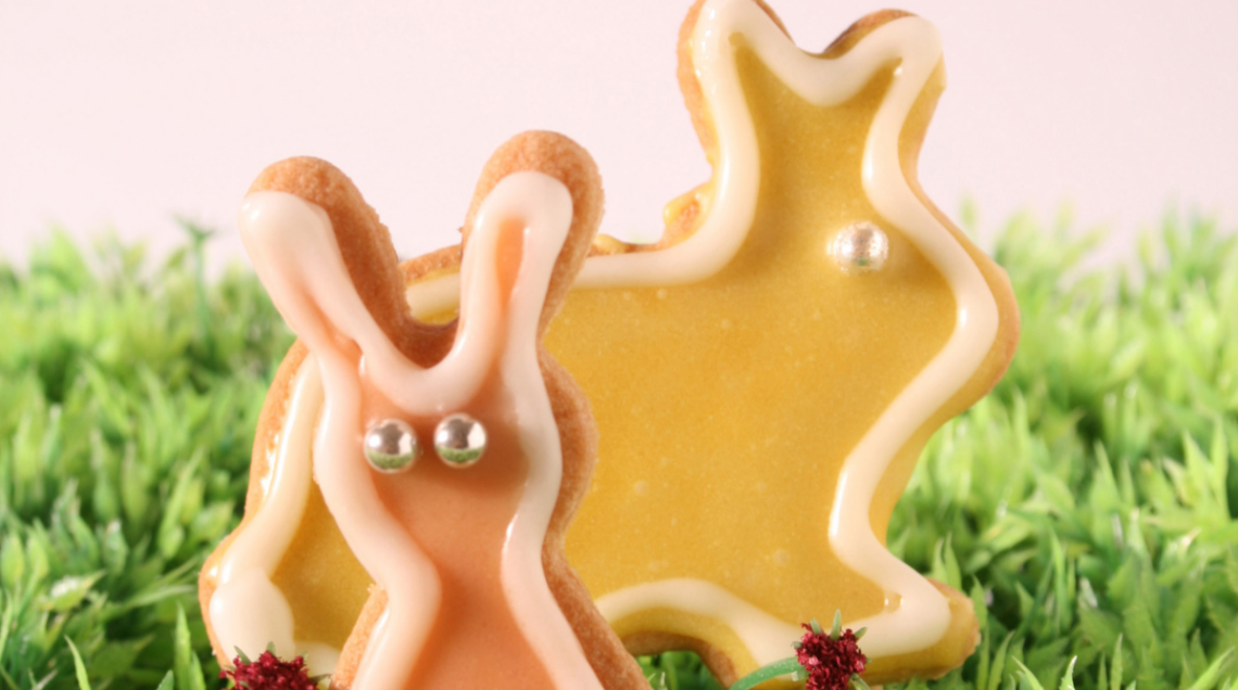 Due biscotti di pasta frolla a forma di coniglio decorati con glassa colorata e confetti argentati su un prato finto