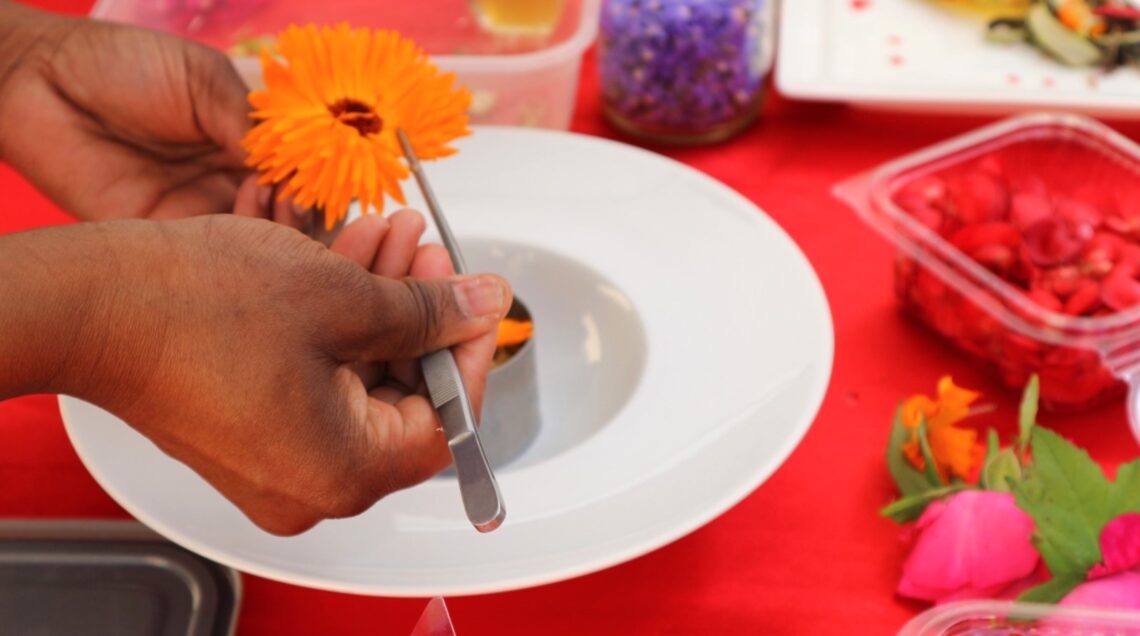 Chef che stacca i petali da un fiore di calendula arancione con una pinza professionale.