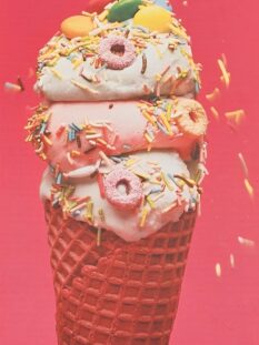 Primo piano di un cono gelato a tre gusti (menta, fragola e vaniglia) decorato con piccoli donut colorati, zuccherini multicolore e lenti di cioccolato su sfondo rosso vivace.