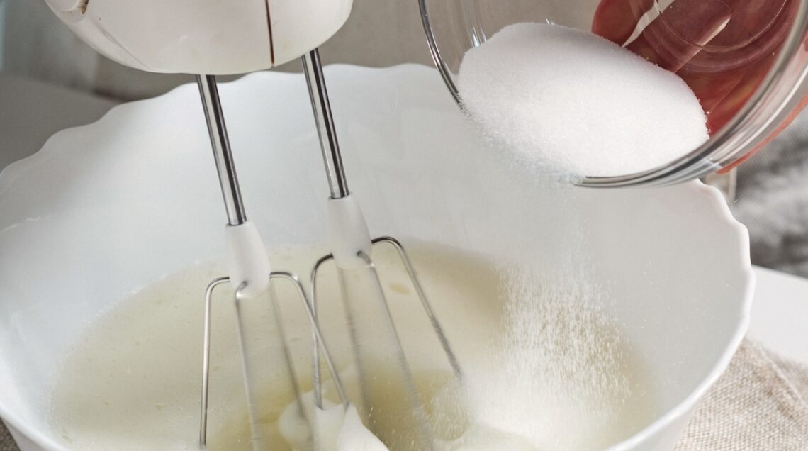 ciotola con albumi, zucchero e sbattitore elettrico