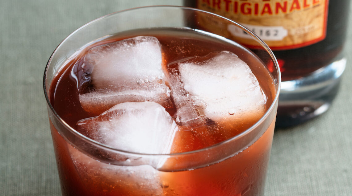 bicchiere con cocktail negroni e ghiaccio e bottiglia di liquore