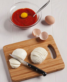 Fettine di mozzarella su tagliere, recipiente bianco con passata di pomodoro e uova
