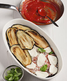 Terrina di parmigiana di melanzane con mozzarella e pentola con passata di pomodoro