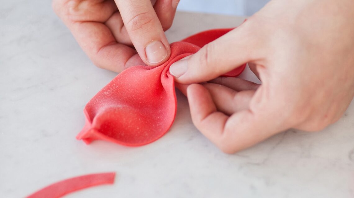 mani che modellano della pasta di zucchero rossa