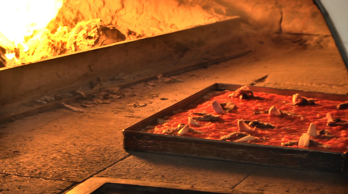 Sardenaira in teglia all'interno del forno durante la cottura, con il pomodoro che bolle e l'impasto che diventa dorato.