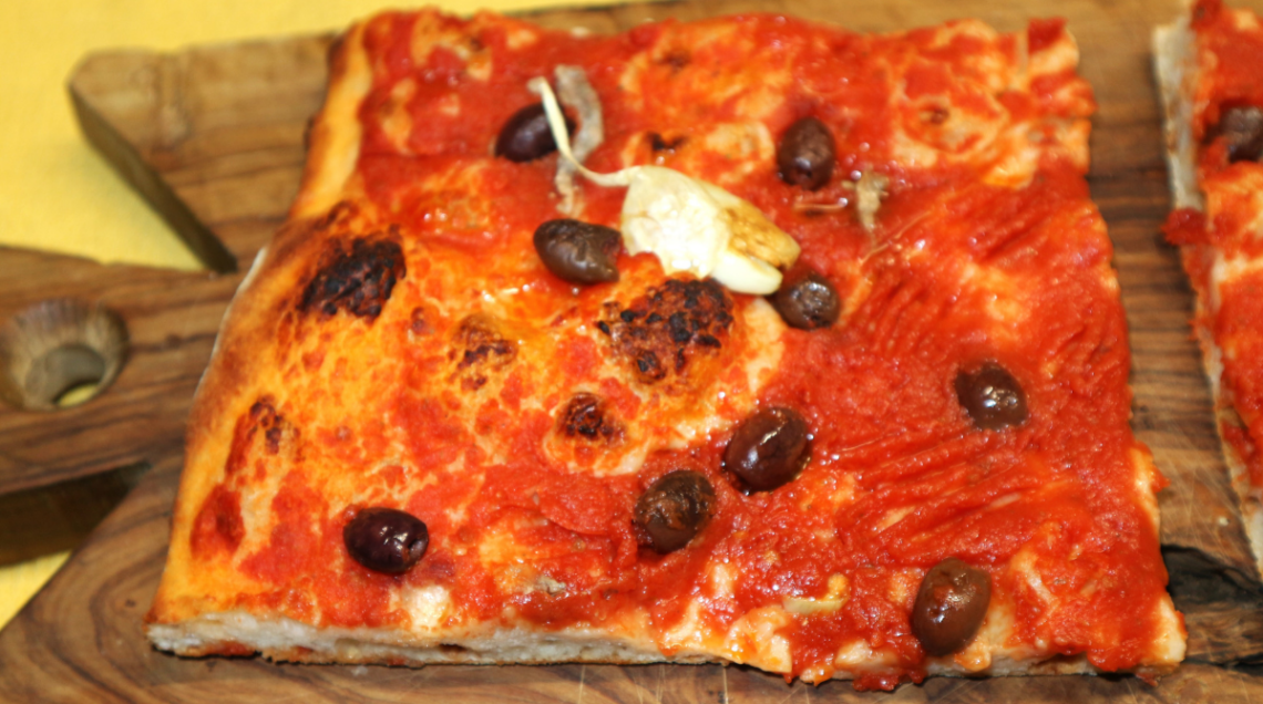 Un trancio rettangolare di Sardenaira alla sanremasca adagiato su un tagliere di legno rustico, pronto per essere servito