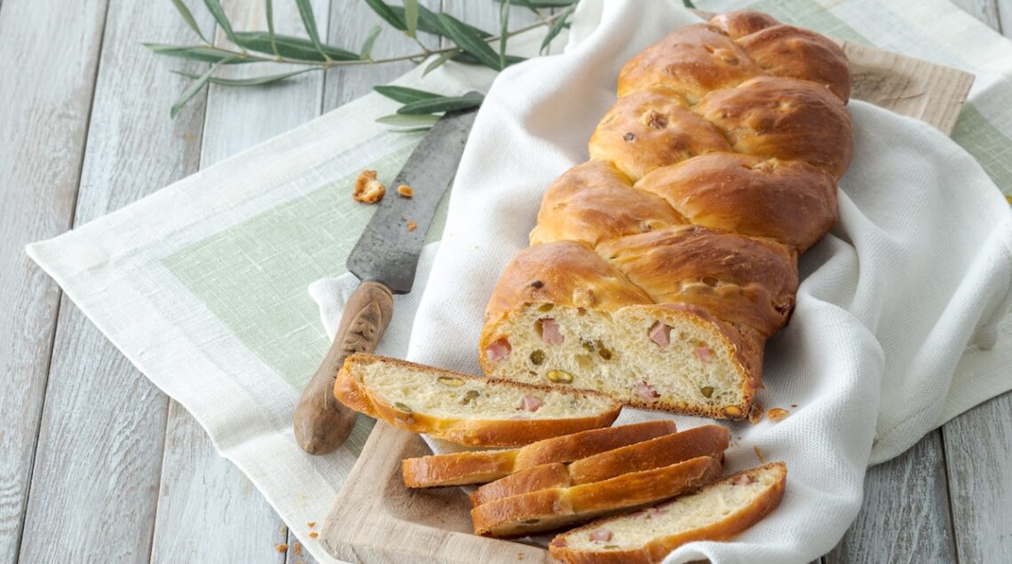 treccia di pane con olive e mortadella parzialmente affettata su un telo bianco