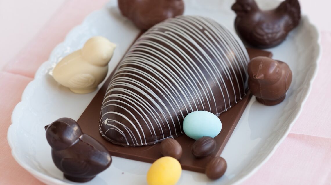 mezzo uovo di Pasqua decorato con fili di glassa bianca circondato da ovetti e pulcini di cioccolato