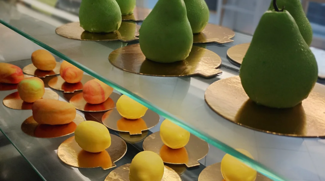 Vetrinistica di pasticceria con dolci a forma di pere verdi e piccoli limoni o albicocche.