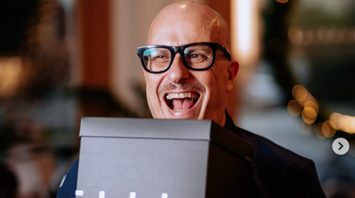 Paolo Brunelli sorride con entusiasmo tenendo una scatola regalo nera