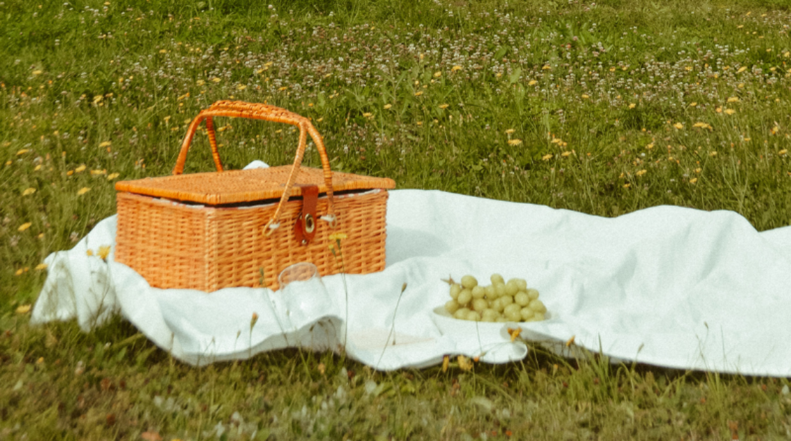 Cesto da picnic in vimini e uva su una tovaglia bianca in un prato fiorito