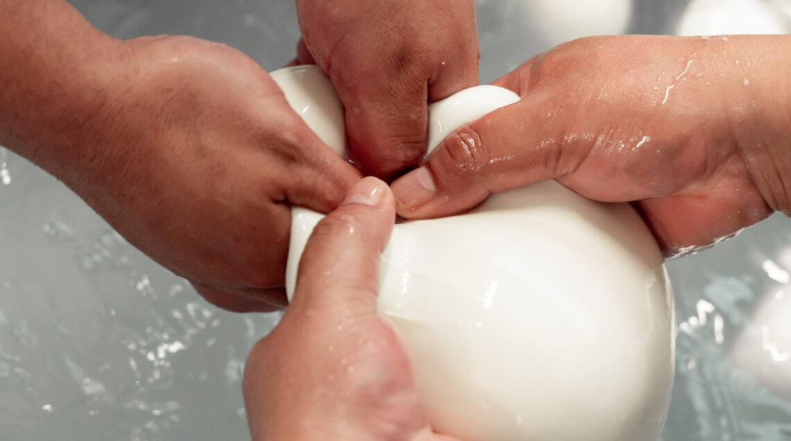 Mani esperte che lavorano e mozzano a mano una pasta filante bianca sopra una vasca d'acqua. 
