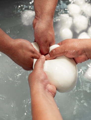 Mani esperte che lavorano e mozzano a mano una pasta filante bianca sopra una vasca d'acqua. 