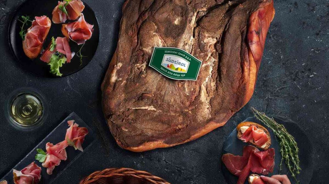 baffa di speck alto adige igp su tavolo con piatti con fette affettate