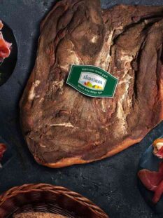 baffa di speck alto adige igp su tavolo con piatti con fette affettate