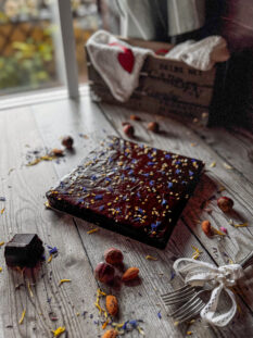 torta quadrata alle carote con glassa al cioccolato, decorata con granella di nocciole e fiori