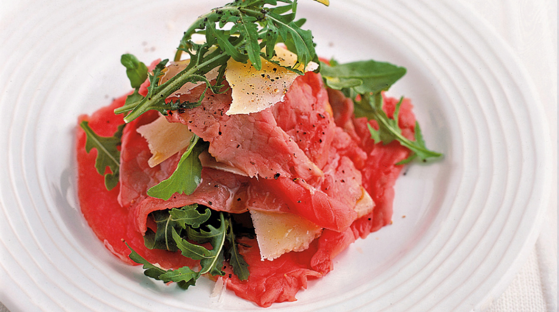 carpaccio di vitello con rucola e formaggio su piatto bianco